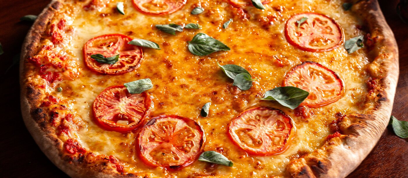Hele pizza met tomaat, gesmolten mozzarella en basilicum — representatief beeld.