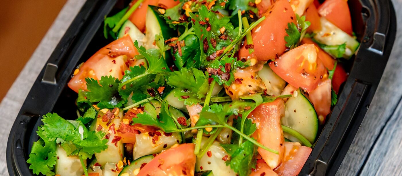 Versgesneden salade van tomaat, komkommer en kruiden in een meeneembakje — representatief beeld.